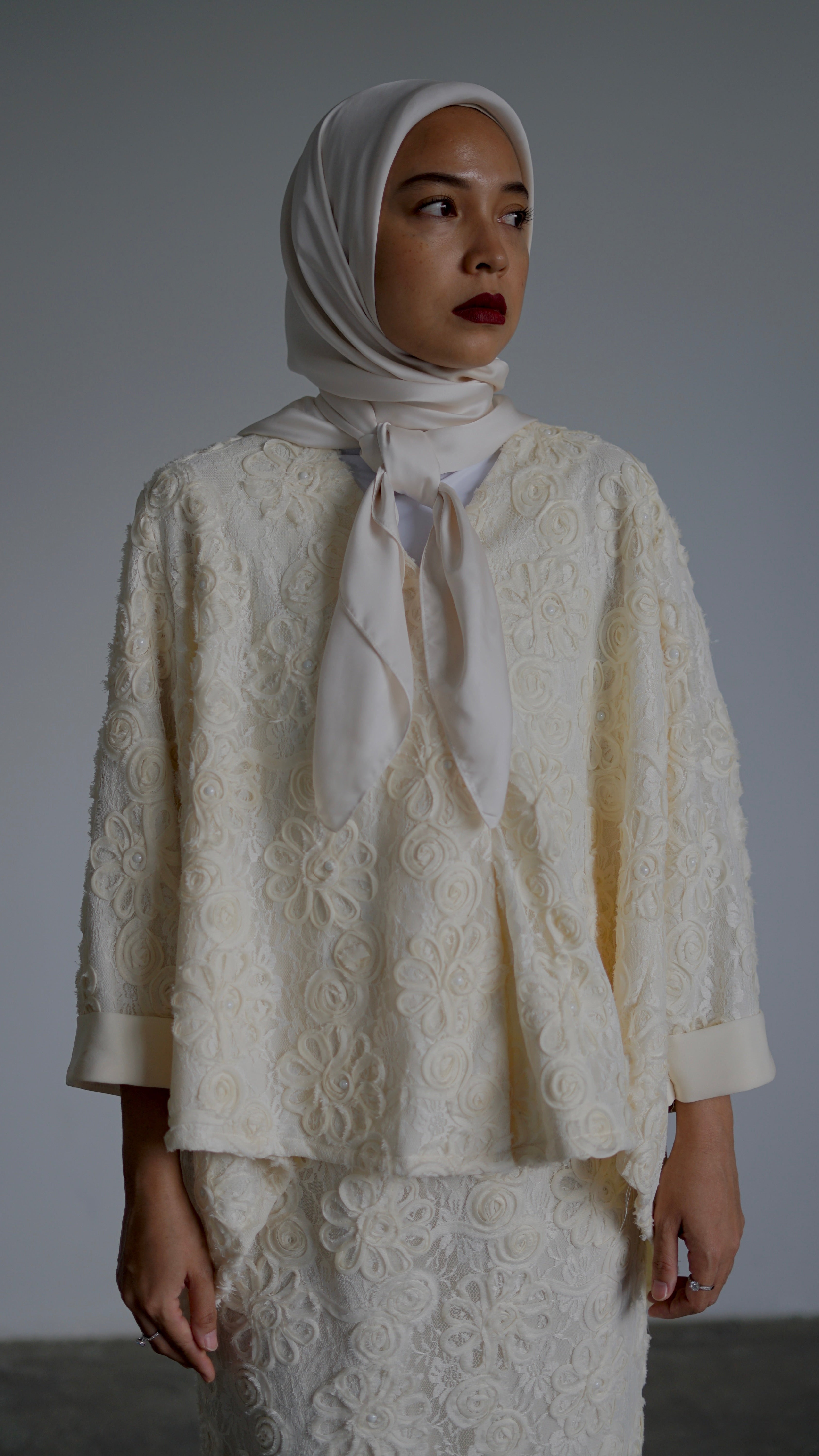 Woman wearing a white lace outfit against a plain background